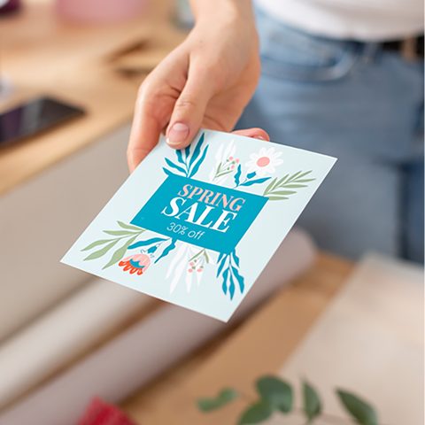 A hand holding a printed spring sale flyer